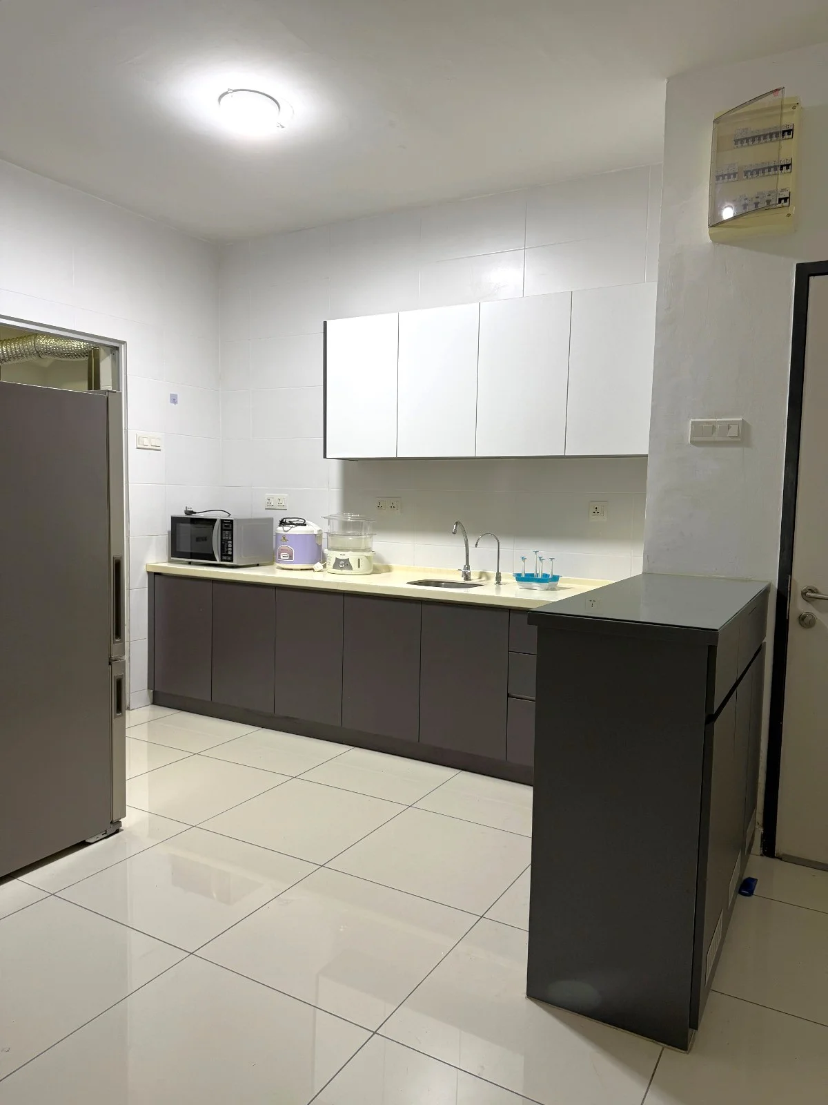Kitchen features: white upper cabinets, grey lower cabinets, laminate countertop, single-bowl stainless-steel sink, chrome pull-down faucet, built-in microwave, freestanding fridge, ceramic tile flooring, recessed ceiling lights, wall-mounted electrical panel, neutral wall tiles, open shelving, kitchen appliances; style: modern.